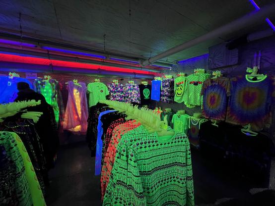 Racks fluorescents de Cyberdog : Une rangée de vêtements fluorescents aux motifs néons dans la boutique Cyberdog à Camden. A row of fluorescent clothing with neon designs inside the Cyberdog shop in Camden. Una fila di vestiti fluorescenti con design al neon all'interno del negozio Cyberdog a Camden.