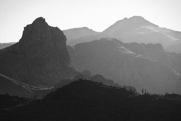 A black and white image of a prominent ridge in the foreground with other ridgelines fading off into the distance. The image works from darker layers in front to brighter layers in the back. 