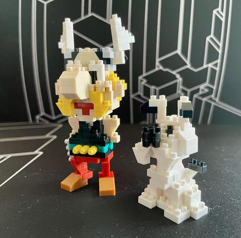 Image features two colorful block figures: one is a humanoid character with blonde hair and large horns, wearing a multicolored outfit, and the other is a small white creature with black details, resembling a dog. The background is a geometric black design