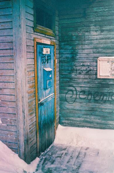 The photo shows the entrance to a wooden house with a blue, old door, a beautiful shabby texture at the door and at the wall of the house.