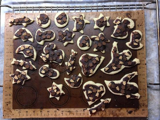 Decorated cookies of various shapes - witches, sharks, ghosts, hearts, bells, stars, squirrels - lying on a brown silicon mat