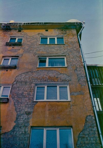 In the photo, the wall of an old house with peeling plaster from under which the brickwork peeks out.