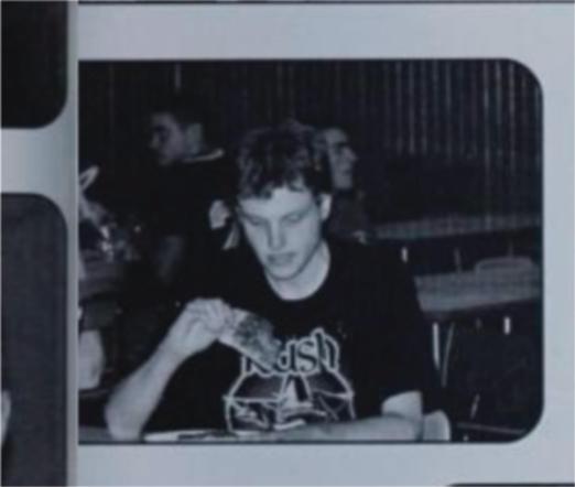 A monochrome picture of me taken candidly my senior year. I'm not aware of the photo being taken and am looking glumly at a slice of pizza. I am wearing, appropriately, a Rush T-shirt from the 30th anniversary tour because it was an out of uniform day. I am completely alone at my table.