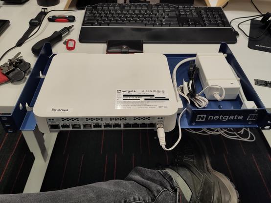 A Netgate 6100 router running pfSense with a rack mount accessoire sitting on a desk.