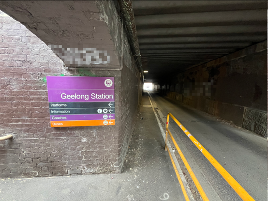 Road tunnel with a narrow footpath. A sign says Geelong station is off to the left.