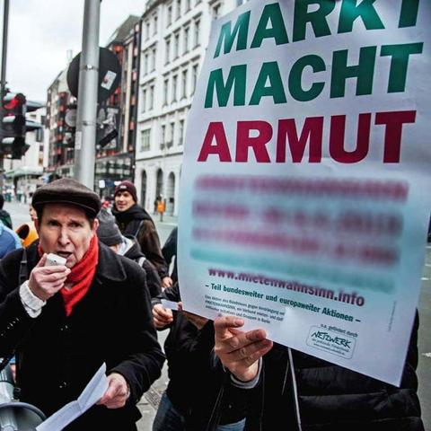 Ein Mieter mit Mikrophon protestiert lautstark gegen die Zustaende, ein anderer haelt ein Plakat mit dem Slogan "Markt macht Armut" im Vordergrund

