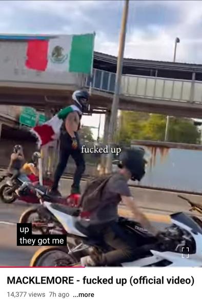 Screen grab from Macklemore video FUCKED UP. we see comrades on scooters at street action waving flags of resistance to the fascist takeover
