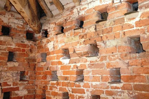 Red brick walls inside the dovecote with square holes for nesting birds and slate landing platforms.