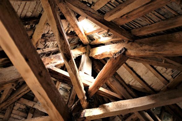 In the roof space of the building are a tangle of beams, some original and others later props and and crossbeams. There are a few holes.