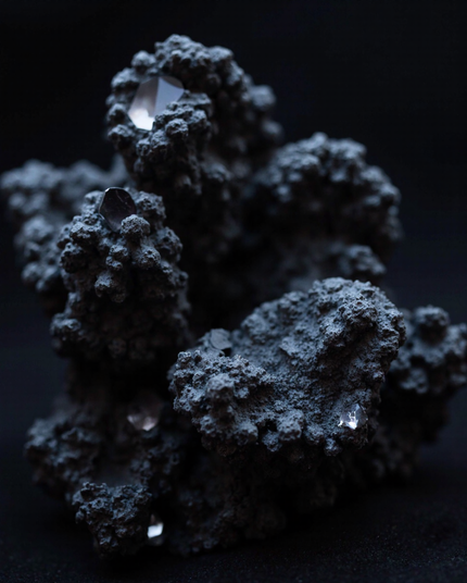 A close-up of a rugged, dark mineral formation cradling embedded reflective crystals. The interplay of rough textures and glistening facets evokes a sense of mystery and contrast.