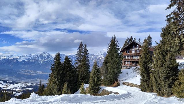 View over the snowy alps, a cottage in the front and the tobbogan run downhill.