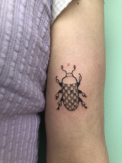 Tatouage au handpoke sur un bras d’un scarabée à motif de damier