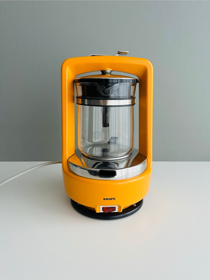 A vintage Krups coffee maker in bright yellow with a glass pot, reflecting a mid-century modern design.
