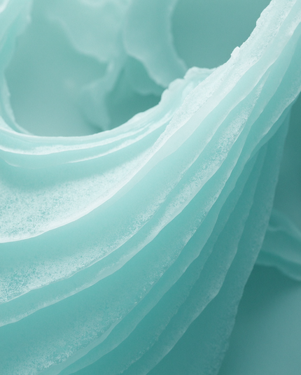 A close-up of delicate, layered formations in soft turquoise, resembling frozen waves or eroded mineral surfaces. The image conveys a sense of fluidity captured in stillness.