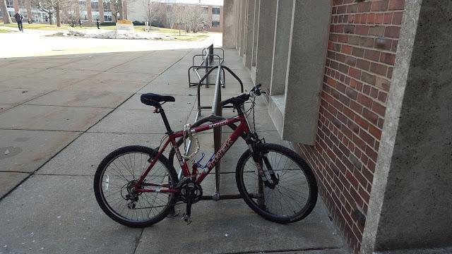 Bike chained up at school. It's the only bicycle on the rack.