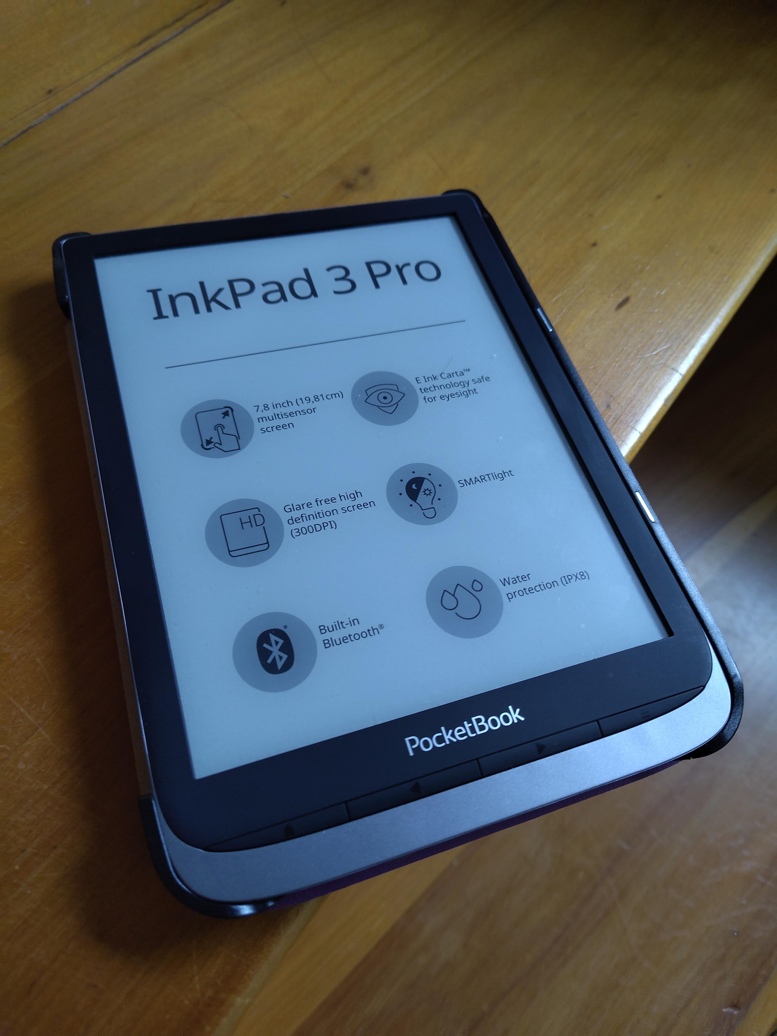 Picture of an InkPad 3 Pro eBook Reader placed on a wooden surface. The display is in sleep mode, advertising various features of the device.