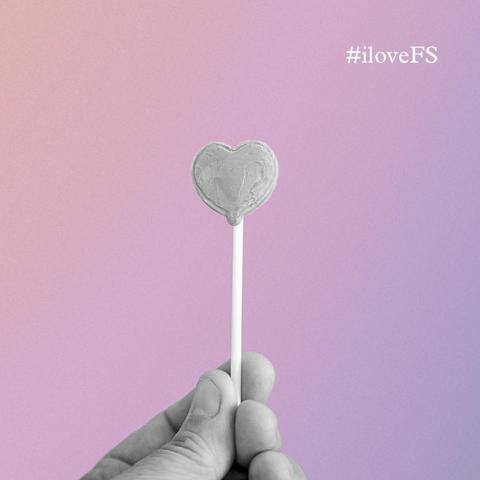 Das Bild zeigt eine Hand, die einen Lolli in Herzform hält. Oben steht ein Hashtag: #iloveFS