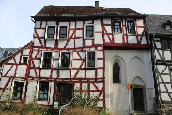Fachwerkhaus über drei Etagen, etwas schief und krumm, mit roten Balken und weißen Gefachen. In der rechten Haushälfte ist ein Bereich über zwei Etagen etwas zurückgesetzt und grau verputzt. Ein Kirchenfenster lässt die ursprüngliche Nutzung erahnen. Darüber befindet sich wieder eine Etage mit Fachwerk. Fachwerkteil und ehemalige Kapelle haben ein gemeinsames Dach. 
Der Vorgarten ist etwas verwildert.
Rechts steht im Anschluss ein weiteres Fachwerkhaus, dort war früher das Schiff der Kapelle. 
