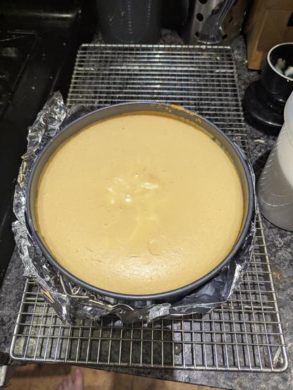 Cheese cake fresh out of the oven sitting in a spring form on a cooling rack