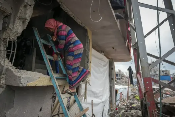 A woman descends a blue ladder from an opening in the wall.