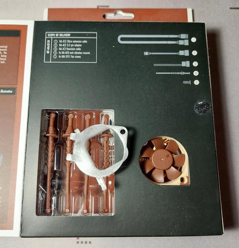 Man sieht die aufgeklappte Verpackung eines Noctua Lüfters. In der Verpackung liegen Gummi-Abstandshalter, die den Lüfter leiser machen sollen und rechts daneben sieht man den Noctua Lüfter. Auf der Verpackung liegt ein 3D gedrucktes Teil, das zum Einbau in die Sega Dreamcast verwendet werden soll.