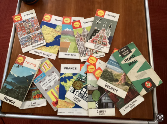 A bunch of mid-century gas station road maps of Europe, spread out on a modern wooden table