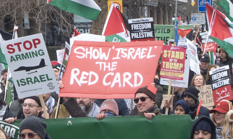 compact crowd, people carrying a 'show Israel the red card', Man in front has a red card on his wooly hat