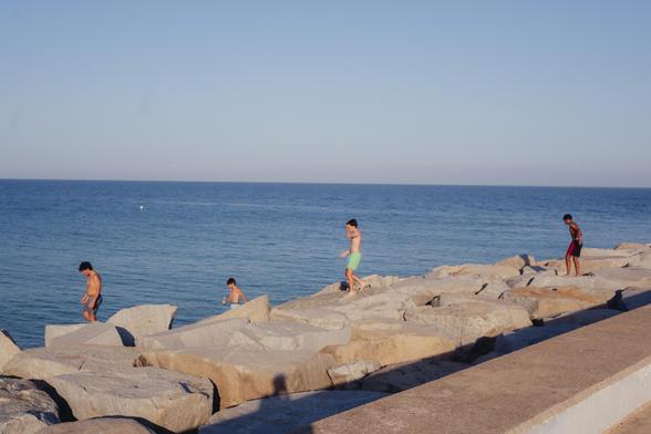 Photograph of some children walking on the rocks next to the port of Mataró, ready to jump into the sea, which can be seen in the background. In the foreground you can see my shadow when I took the photo :)

Fotografía de unos niños andando por las rocas junto al puerto de Mataró, dispuestos a saltar al mar, que se ve de fondo. En primer plano se ve mi sombra al hacerles la foto :)