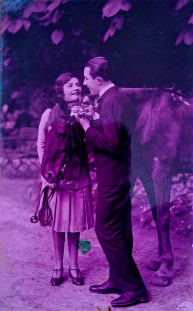 Photography of a woman and a man looking warmly at each other, between the two of them there is a brown horse. He is holding a bouquet of flowers.