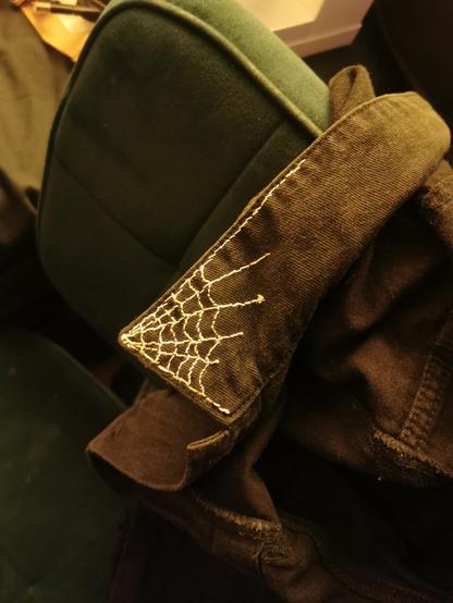 sewn spiderweb with white thread onto the collar of a black denim jacket