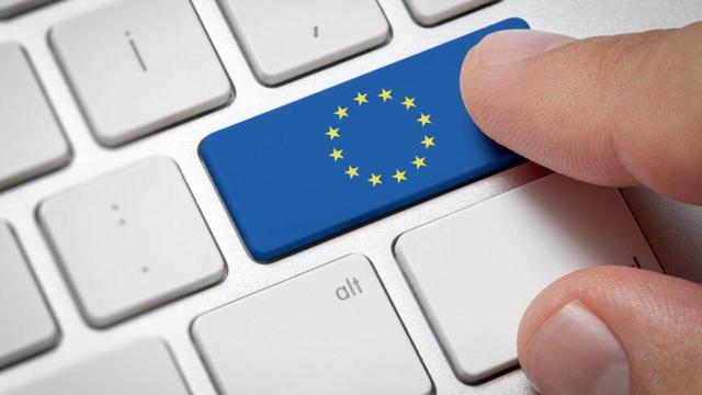 A finger presses a key on a computer keyboard. The key is blue with the European Union flag, a circle of twelve yellow stars on a blue background.  The surrounding keys are white, and the "alt" key is visible below the EU key.
