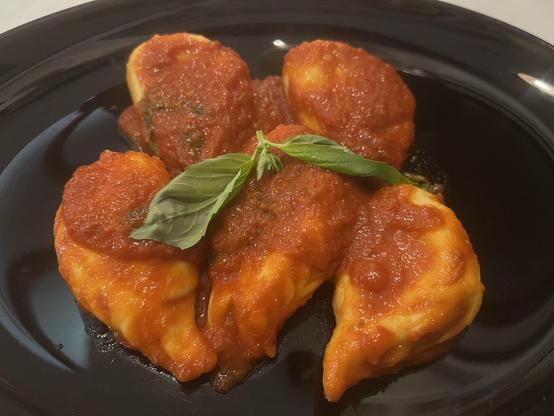 Des Curlugiones (raviolis maison sardes) nappés d'une sauce tomate parfumée et garnis d'une feuille de basilic frais. Homemade ravioli covered in a fragrant tomato sauce and topped with a fresh basil leaf.