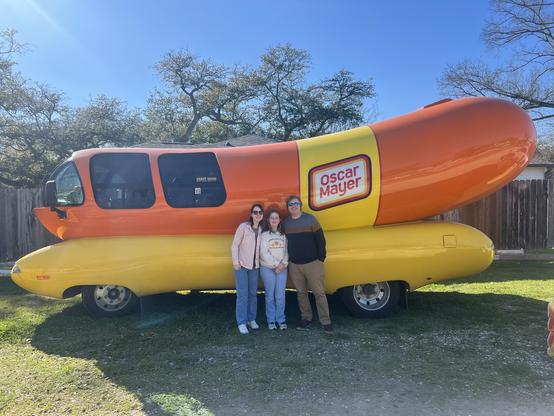A man, woman, and child standing in front of the Oscar’s Mayer Weinermobile.