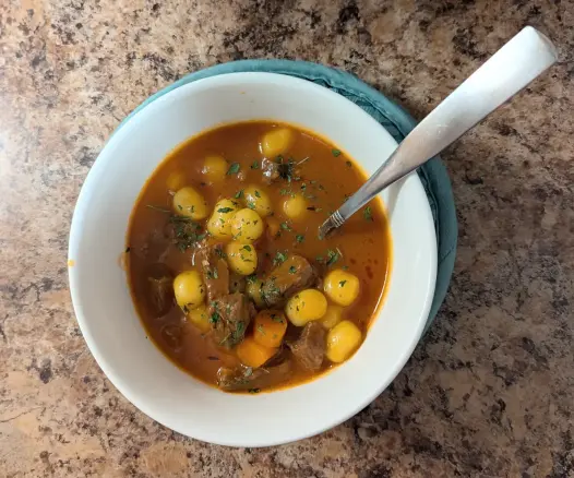 Image shows a white bowl filled with Potato Gnocchi Beef Stew. There's a spoon in the bowl.