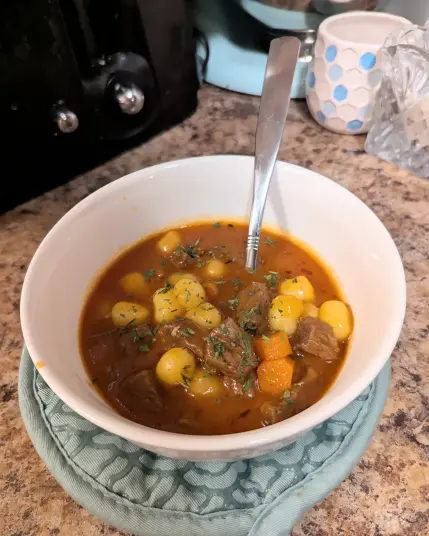 Image shows a close up of a white bowl filled with Potato Gnocchi Beef Stew. There's a spoon in the bowl.
