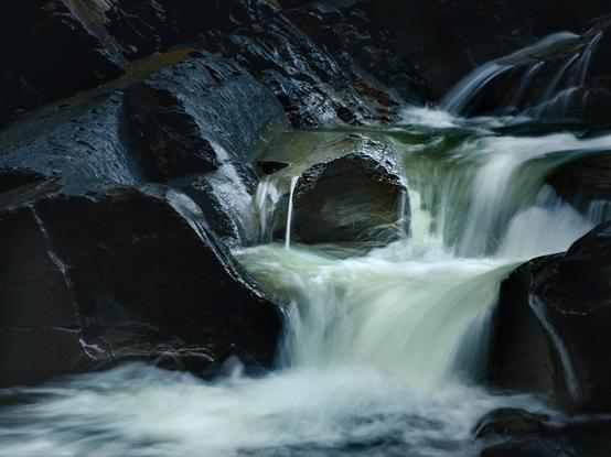 A rock is lodged stubbornly in a waterfall. The water rushes round it, its motion blurred. 