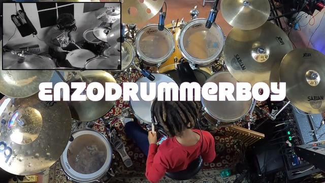 Photograph taken from above and behind of a young boy in a red t-shirt and blue trousers sitting at a drum kit in a recording studio. An inserted monochromatic photograph in the top left corner shows an above and front closer view of the drummer.
Across the photo is the legend in bold typeface, "ENZODRUMMERBOY".

Image from the title card of the YouTube video, "Cows And Bells - Enzo Ursino Drum Solo" - https://youtu.be/e4VNPv0oUBg