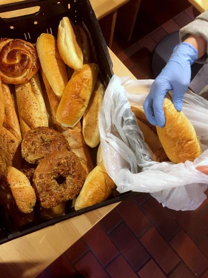 Anika Liekefett entnimmt aus einer Kiste mit türkischen Backwaren ein Baguette und legt es in eine weiße Plastik-Tüte in der bereits einige Brote liegen. Alle Lebensmittel sind gerettet und werden an Bedürftige verteilt.