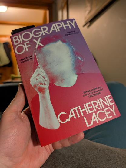 Cover of Catherine Lacey's "Biography of X," featuring a woman holding up a smoky transparent tile in front of her face, making her features indistinguishable