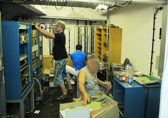 Im  Bild sind 3 Leute zu sehen die an Elektronikschränken Teile demontieren und verpacken .
