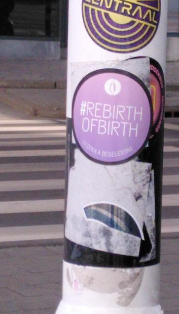 Een ronde paarse sticker op een laterpaal in Alkmaar met witte tekst, in hoofdletters: '#REBIRTHOFBIRTH; 1:1 DOULA BEGELEIDING'