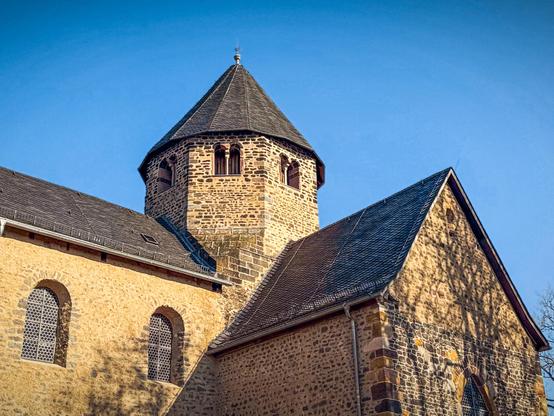 Die Klosterkirche Schiffenberg in Gießen mit romanischer Architektur, Sandsteinmauern und einem achteckigen Turm. Sonnenlicht betont die Struktur, während der blaue Himmel einen klaren Kontrast bildet.