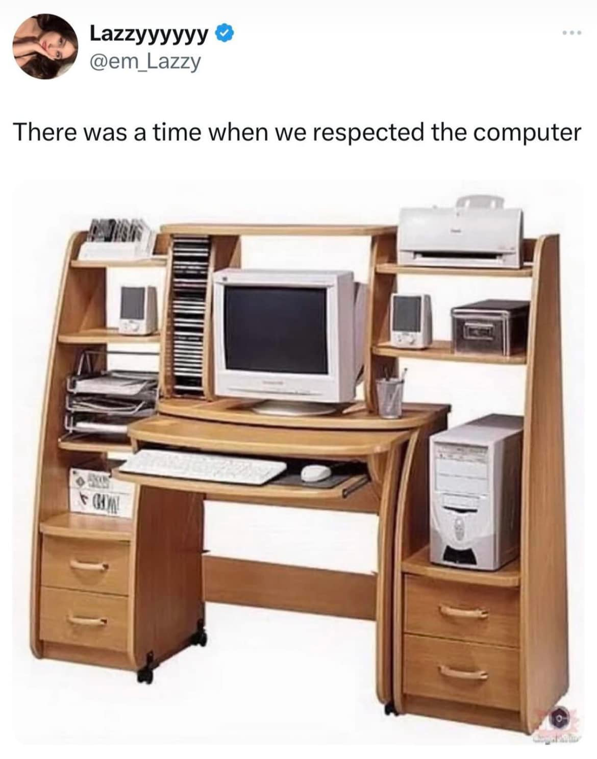 The image is a tweet from the user "Lazzyyyyyy" (@em_Lazzy), which includes a caption that reads:
"There was a time when we respected the computer."

Below the text, there is an image of a classic wooden computer desk from the early 2000s. The desk is well-organized and designed specifically to accommodate an entire desktop computer setup, including:

    A CRT monitor in the center.
    A sliding tray for the keyboard and mouse.
    A dedicated space on the right for a large, beige-colored tower PC.
    Multiple shelves holding CDs, books, and office supplies.
    A printer placed on the upper right shelf.
    Additional storage drawers and compartments for organization.

The image evokes nostalgia, highlighting the era when computers were given dedicated, elaborate furniture setups before the rise of compact laptops and minimalist workspaces.