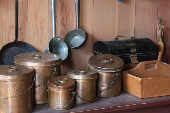 The pots and pans and storage containers and wooden boxes that might be found in the kitchen of a fur trade post.