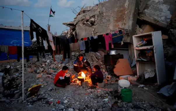 Palestinians sit around a fire amid the rubble of buildings, surrounded by clothing on lines.