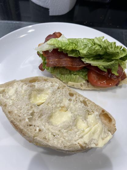 An open BLT with two halves of an M&S Ciabatta with the bottom half covered in slices of crispy bacon, lettuce, and tomato. 
