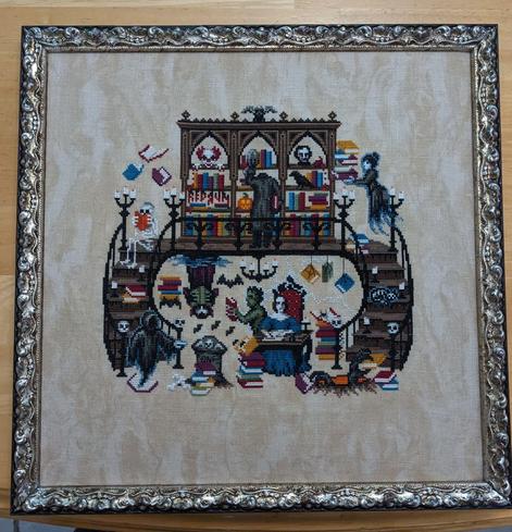 Picture of a framed Haunted Library cross stitch - denizens of the library include skeletons, ghosts, vampires, Frankenstein's monster, Mary Shelley, the headless horseman, and lots of little haunted story details.