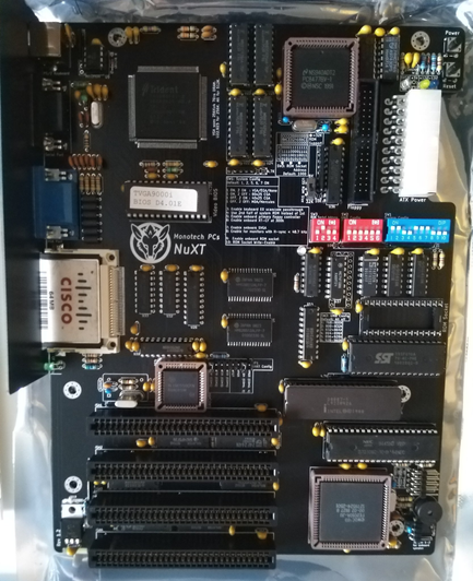 **TL;DR:** A Monotech NuXT motherboard, a modern XT-class board for retro computing, featuring built-in VGA and networking.  

This is a Monotech NuXT Turbo XT motherboard, designed for vintage PC enthusiasts. It has a black PCB with multiple ISA slots for expansion cards, an integrated Trident VGA chip (TVGA9000i), and a Cisco networking module. The board supports a NEC V20 or Intel 8088 processor, visible near the bottom right. DIP switches allow configuration, and an ATX power connector provides modern compatibility. This board enables users to build or restore an early IBM-compatible PC with modern reliability.