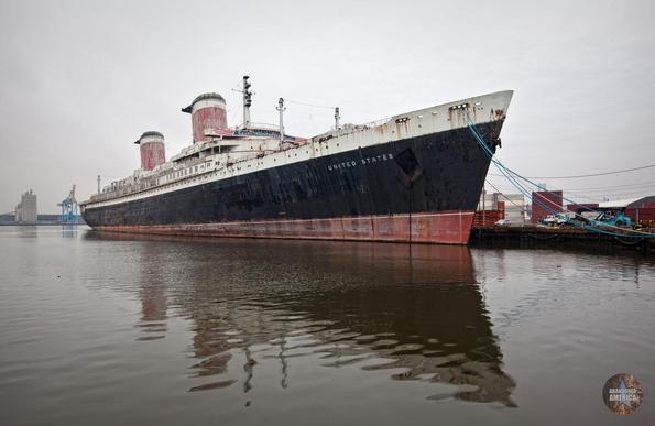 A majestic black, red, and white liner on a gloomy afternoon. The paint is peeling but it still showcases the proud, elegant lines of midcentury ocean liner design. On its side, the words "United States" are visible.
