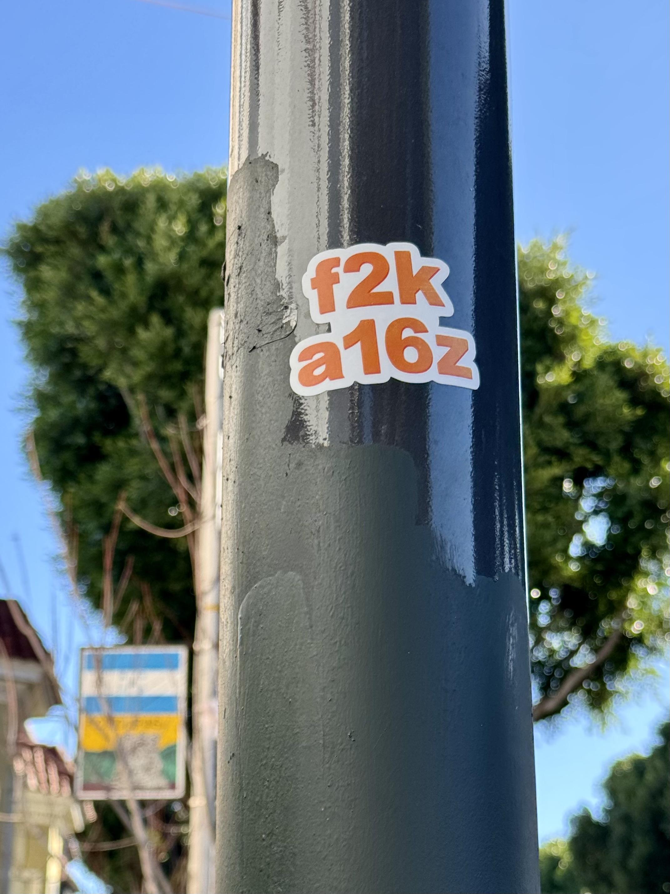 A sticker on a street lamp post. The sticker says "f2k a16z", which is a reference to Andreessen Horowitz, a venture capitalist firm heavily involved in cryptocurrencies, NFTs, and AI. They heavily donated to Trump's campaign and several key Andreessen Horowitz execs have been given roles in Trump's cabinet that will give them power to "regulate" themselves and their competitors.